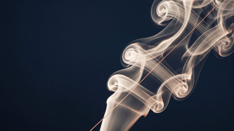 Volutes de fumée ivoire traversées d'un fil de lumière cuivrée sur fond bleu nuit